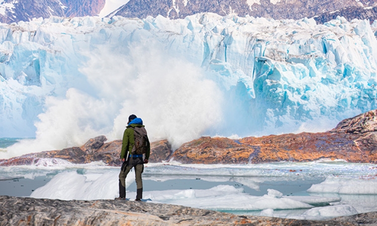 A person stands next to a glacier 