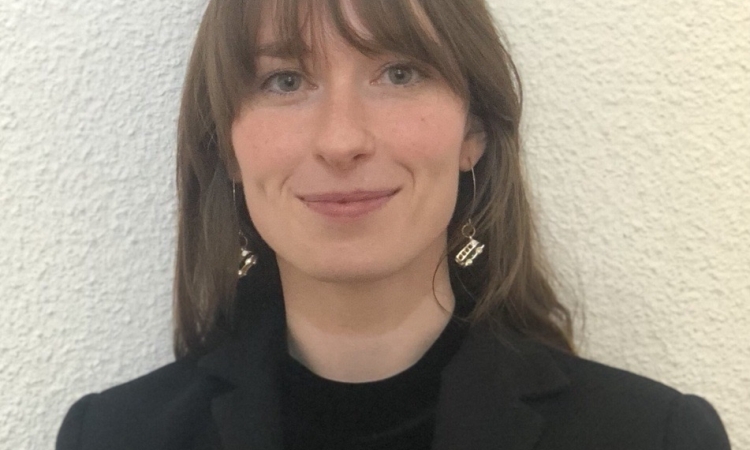 A portrait of Adair Garrett wearing a navy blue blazer with a butterfly pin and a black blouse