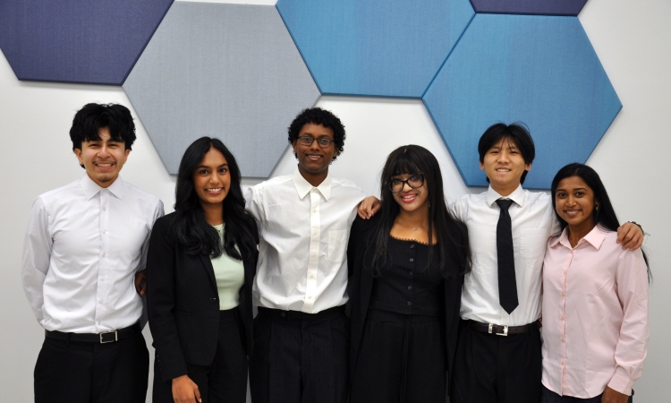 A group of six students poses in front of blue hexagon wall decor 