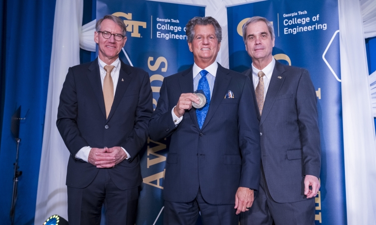 Three men in suits pose with a medal 