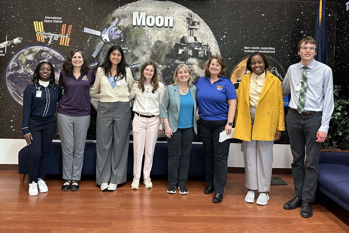 A group of people pose in front of a mural of outer space