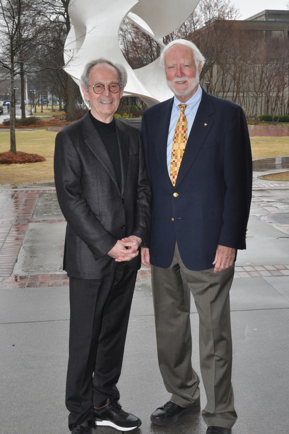 Two men pose in front of a white sculpture