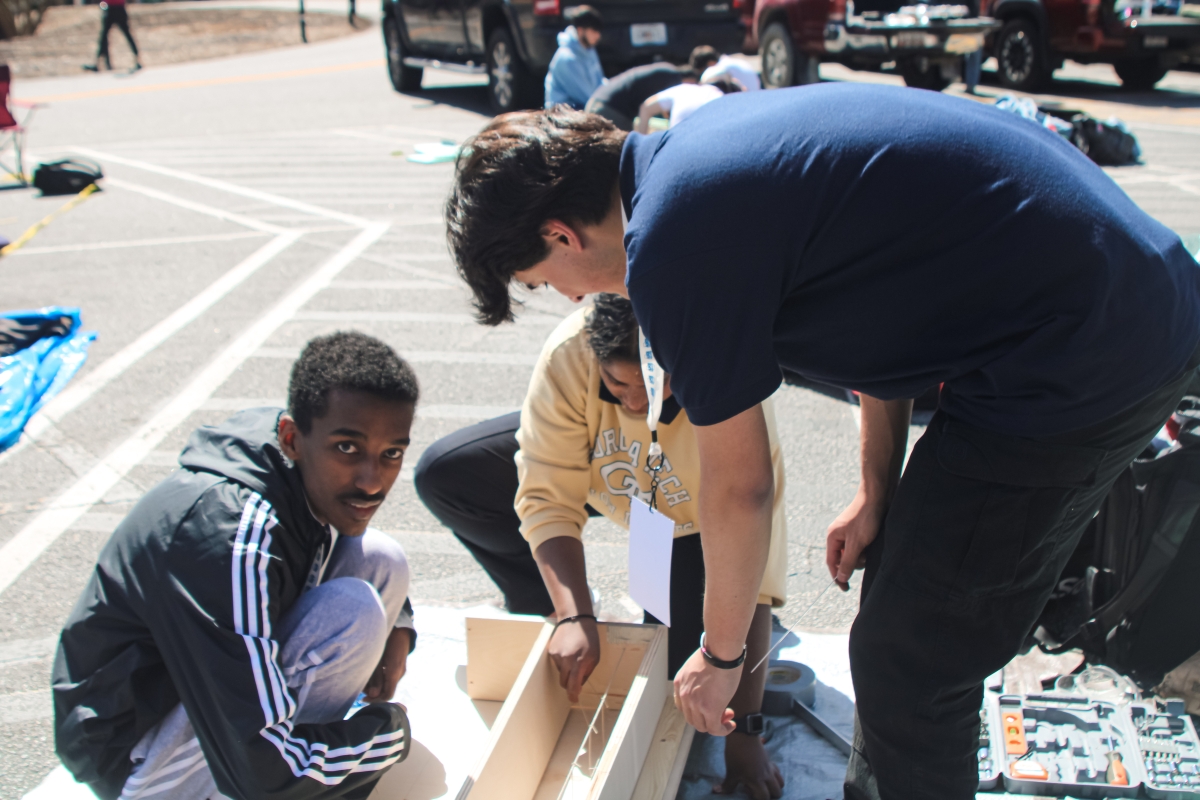 Three students in a parking lot work on the wooden form for a concrete beam.