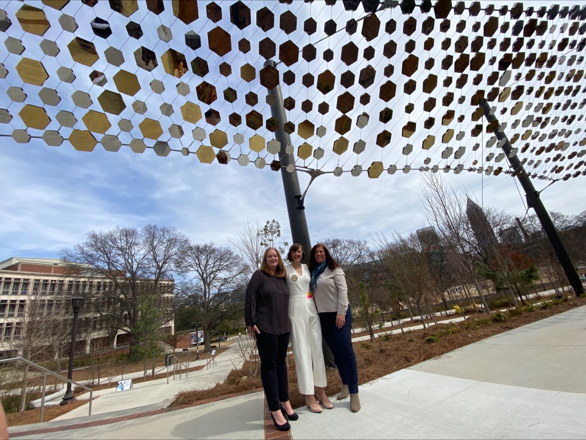 Three women stand beneath a canopy of of mirrored hexagon tiles