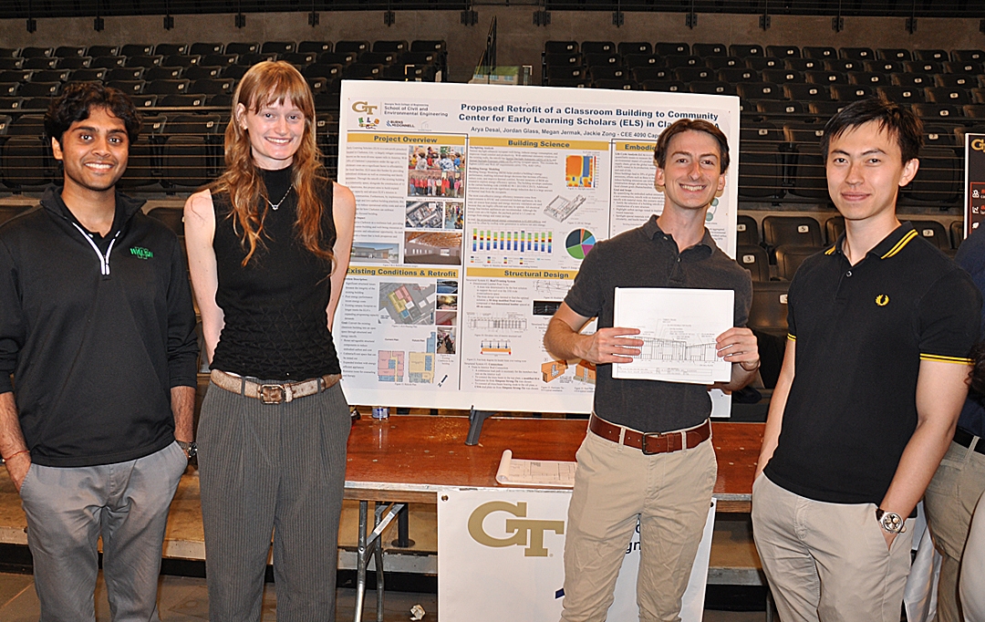 Four students in black shirts pose in front of their Capstone project displayed on an easel.