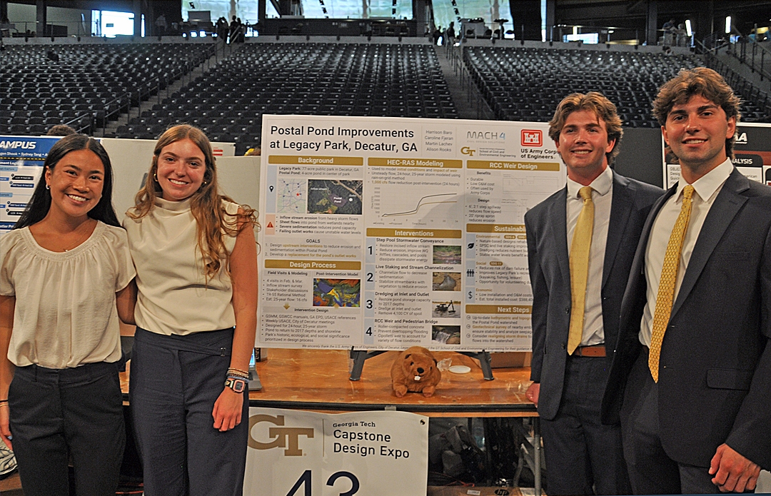 Four students, two women on the left and two men on the right, pose in front of their Capstone project displayed on an easel.