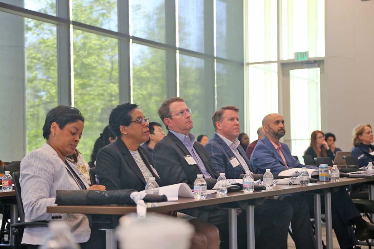 A group of five judges in business attire seated at a table filled with water bottles and notepads