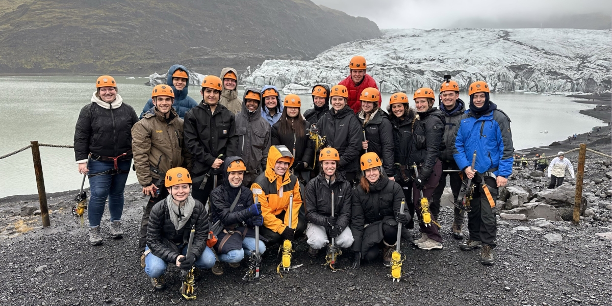 A group in orange helmets in front of a glacier 