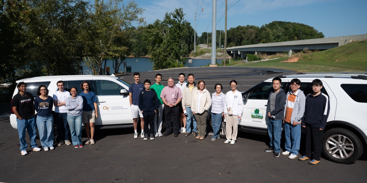 A group of people stands in front of two white SUVs