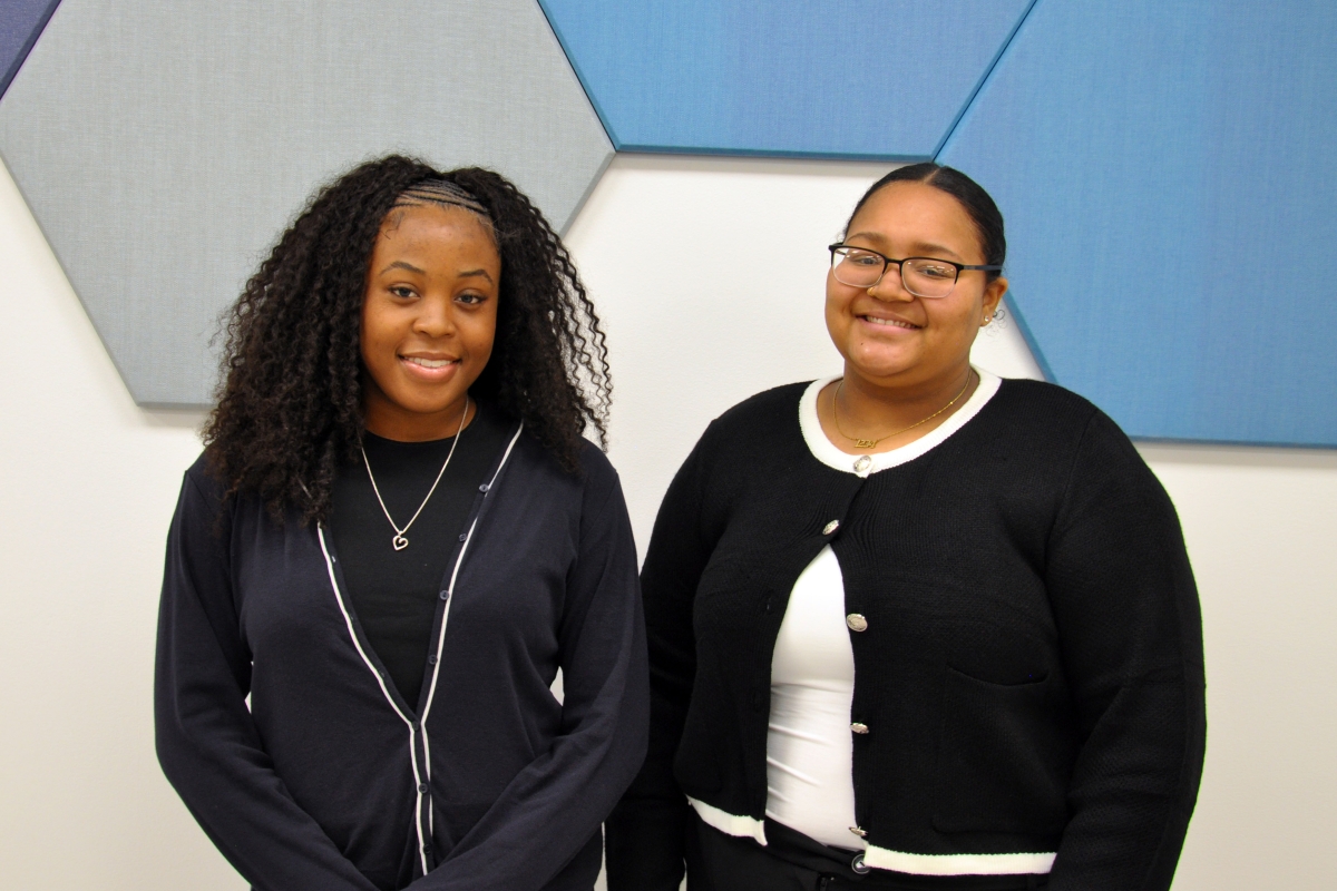 Two women pose in front of blue hexagonal tiles 