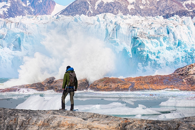 A person stands next to a glacier 