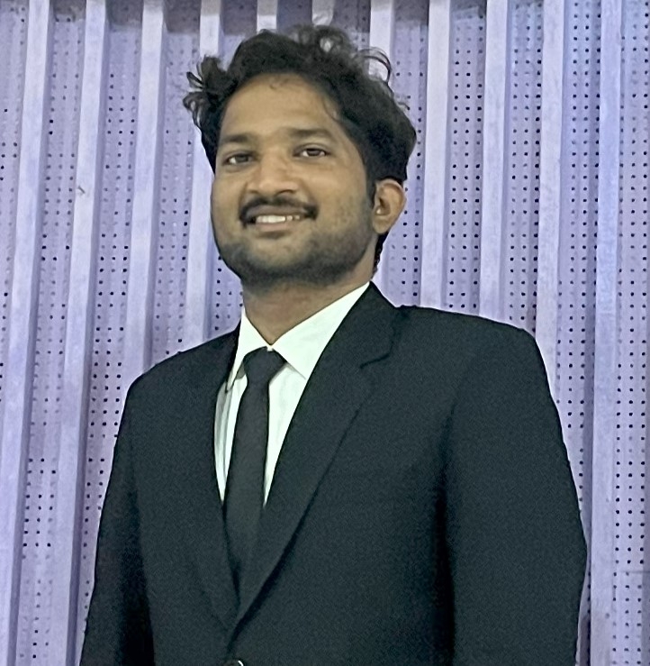 Portrait of Ramoji Rao in a blach suit and tie standing in front of a perforated steel screen